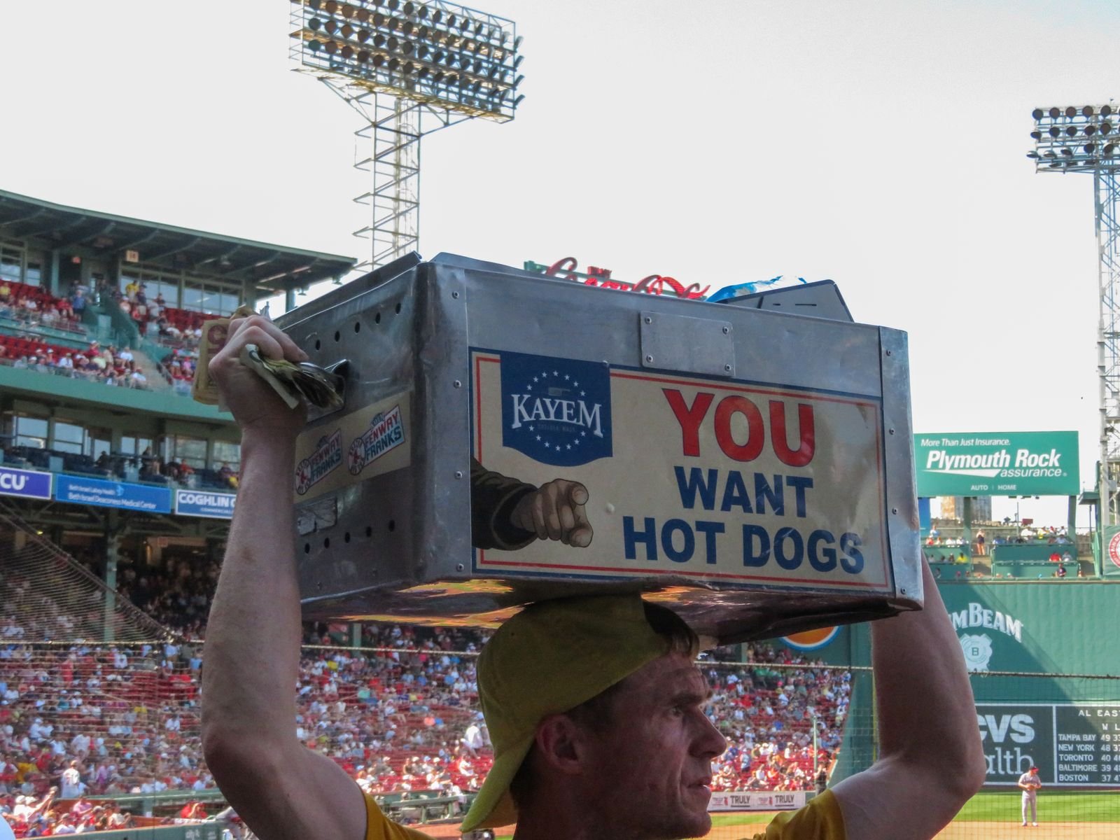 Hot-dog vendor carrying a “You Want Hot Dogs” box in the crowd at Fenway Park, Boston. Photo by Beth Fitzpatrick via Pexels.